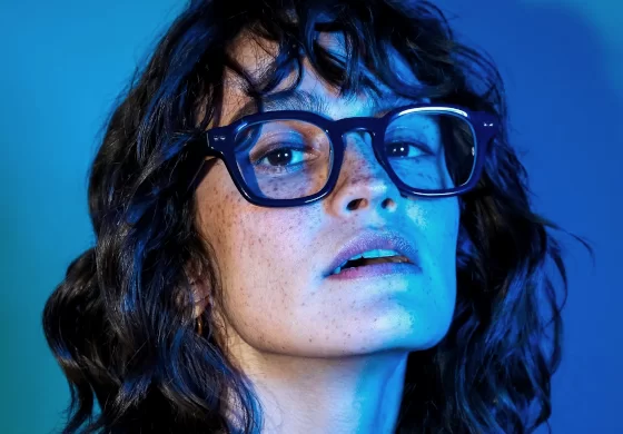 Peter and May Brillen - Frau mit dunklen Haaren, Sommersprossen und großer Brille in blauem Licht